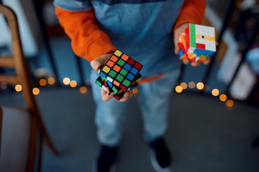 Smiling boy holds puzzle cube in his hands. Toy for brain and logical mind training, creative game, solving of complex problems